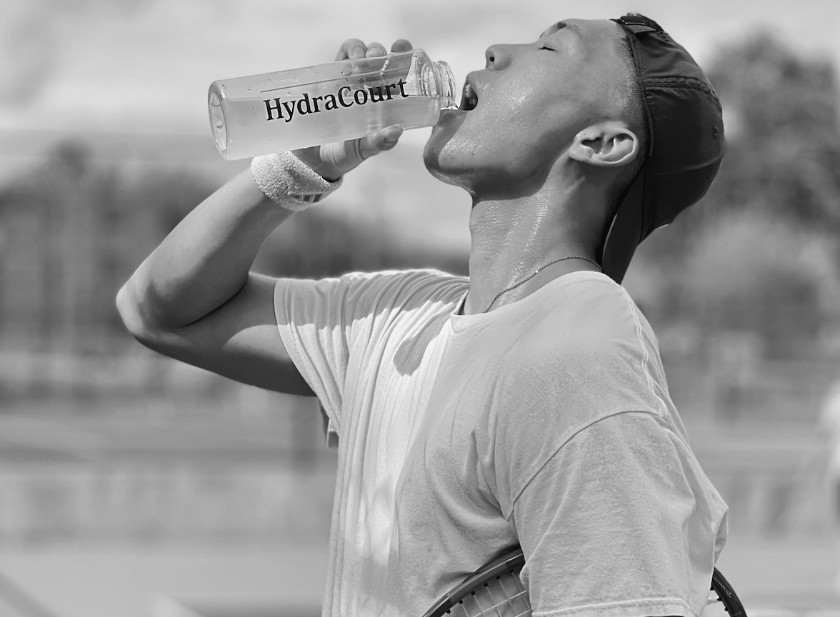 Person drinking from a HydraCourt water bottle outdoors. Refreshing taste and replenishing electrolytes after sweating out. 