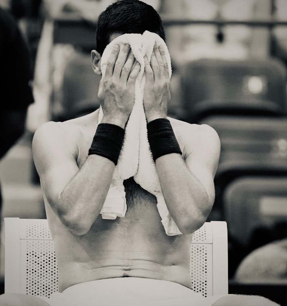Man wiping face with towel in a tennis court setting during a changeover