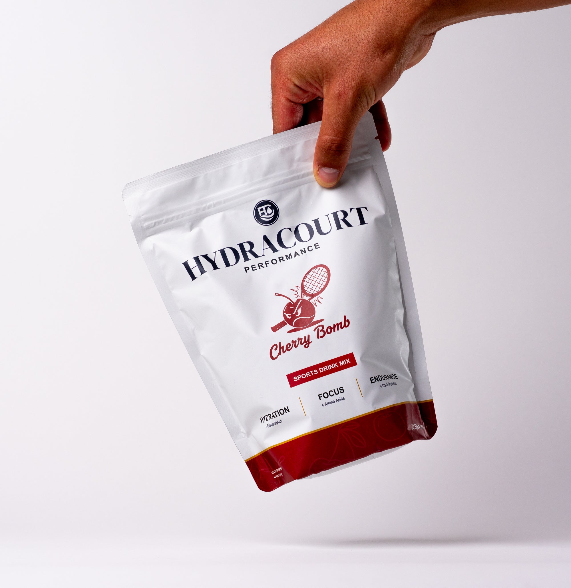 Hand holding a Hydracourt Performance Cherry Bomb sports drink mix package on a white background