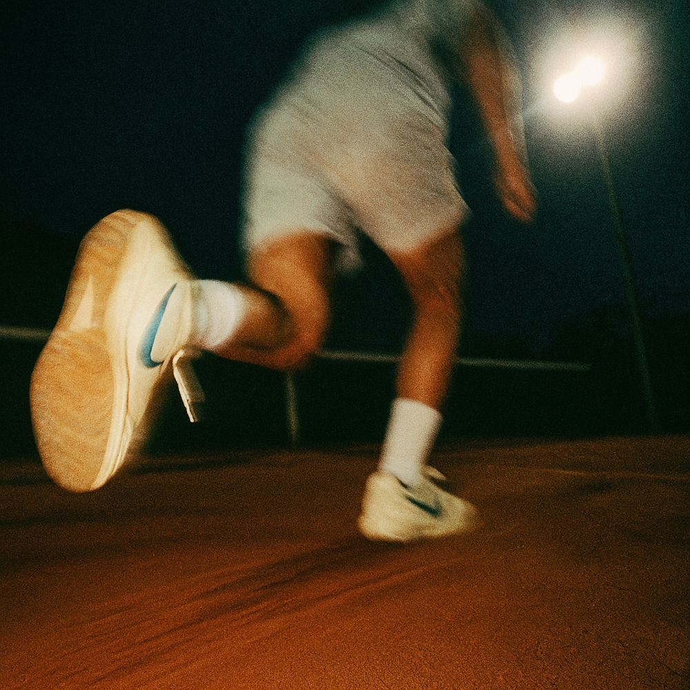 Person playing tennis with a action style background blur, wearing nike shoes. After work at night. 