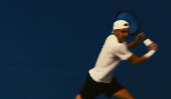Person playing tennis on a blue court. Hitting a one handed backhand.